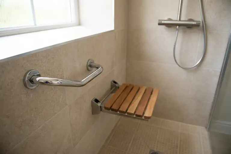 Douche sans seuil équipée d’une barre d’appui, d’un siège rabattable et d’un sol antidérapant